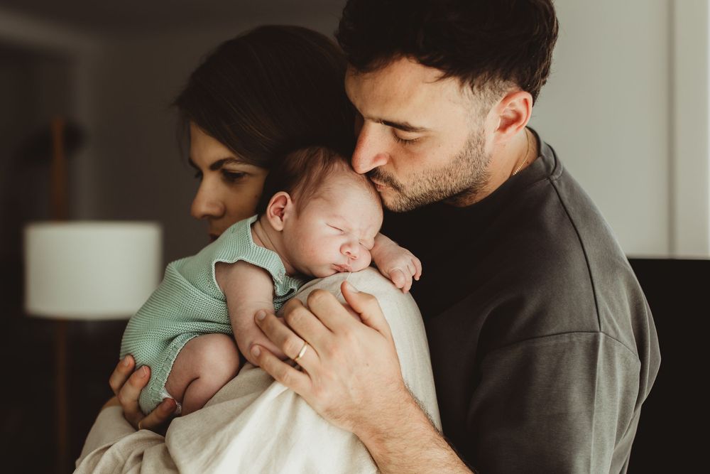 New parents tenderly holding and kissing their newborn baby in a warm, intimate home setting.
