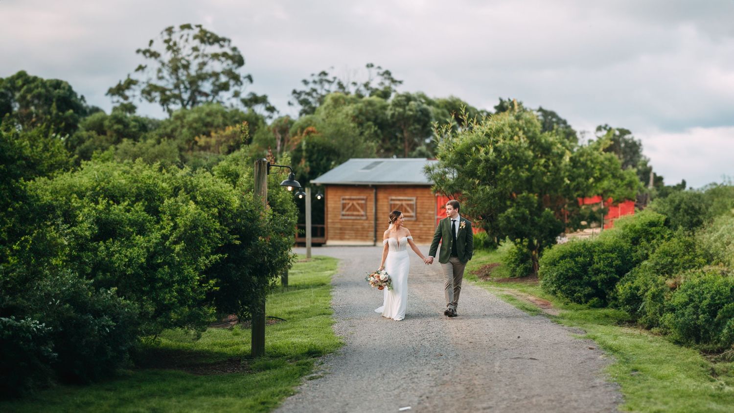 A couple walks down a rustic path with a wooden cabin in the background.