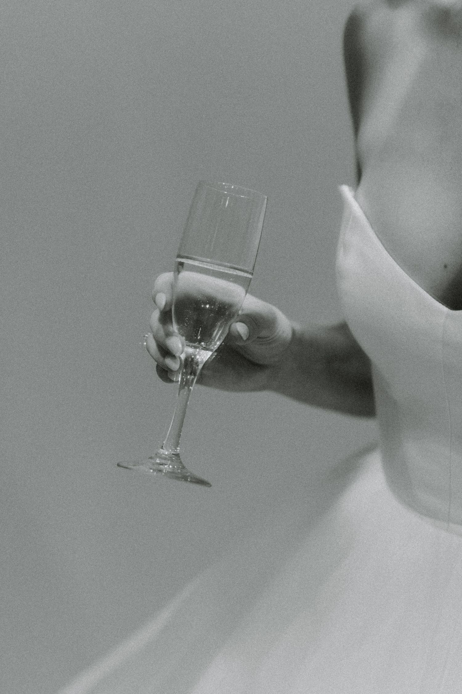 Black and white detail shots of champagne glass held by bride in wedding dress.