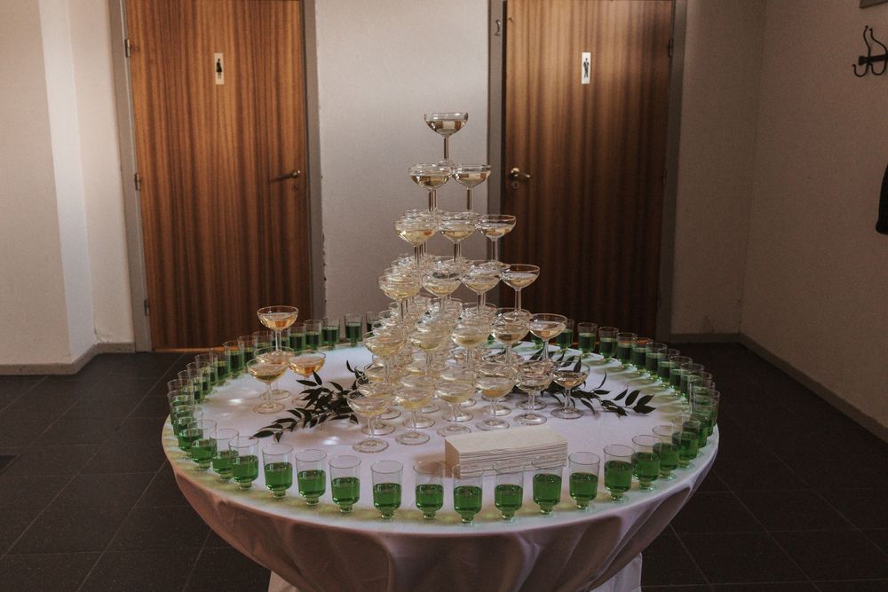 Champagne tower display surrounded by green shot glasses on round table at event.