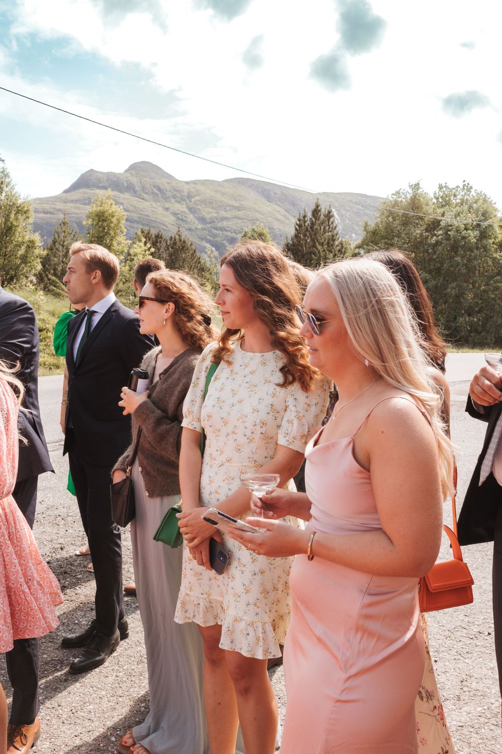 Wedding guests gather on a mountain path wearing elegant dresses and formal wear.