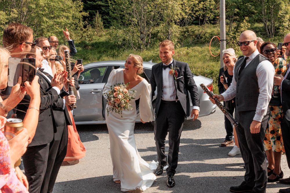 Wedding couple walking down aisle while guests line the sides on sunny day.