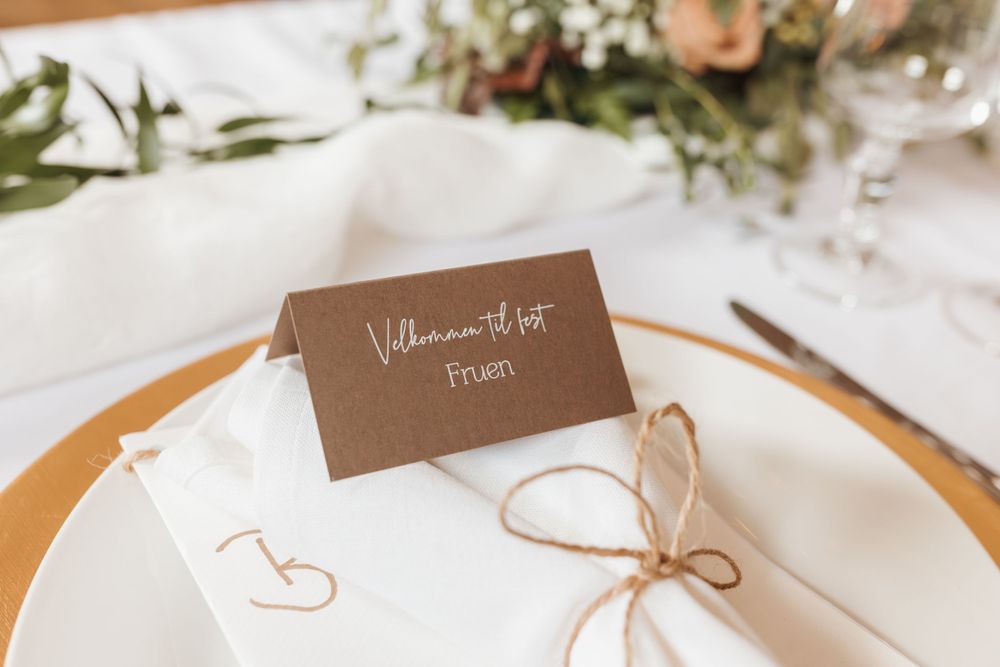 Wedding place setting with brown name card, white napkin, and delicate floral accents.