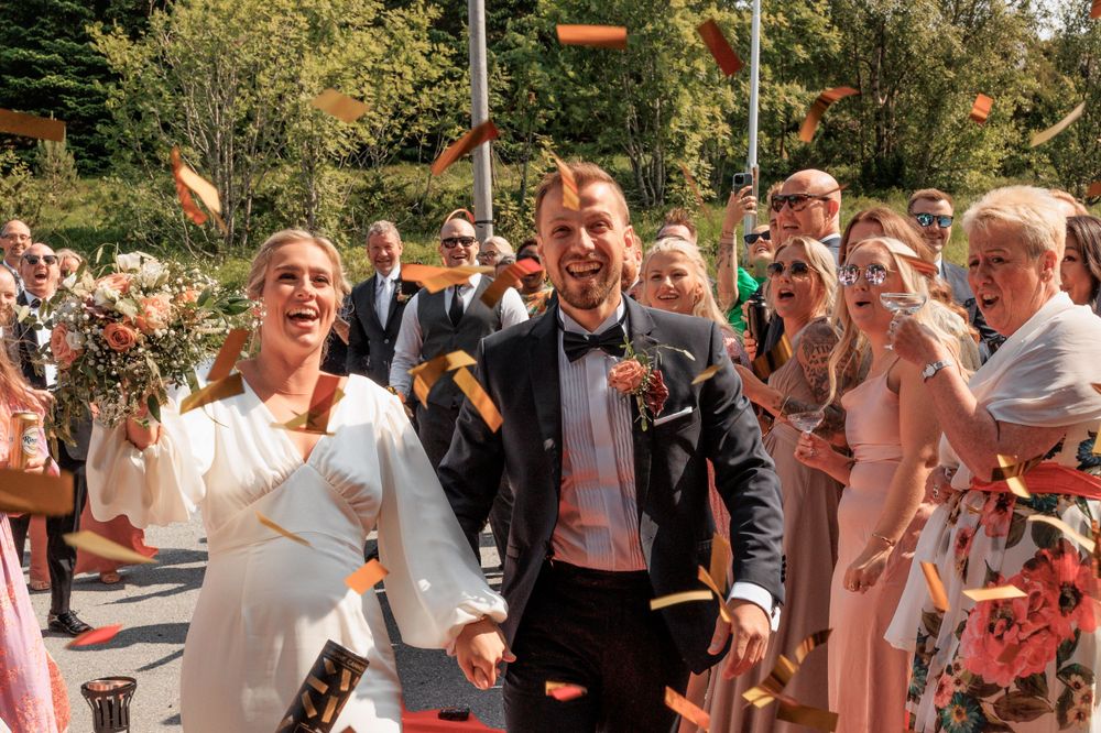 Celebration with confetti as couple walks down outdoor red carpet aisle.