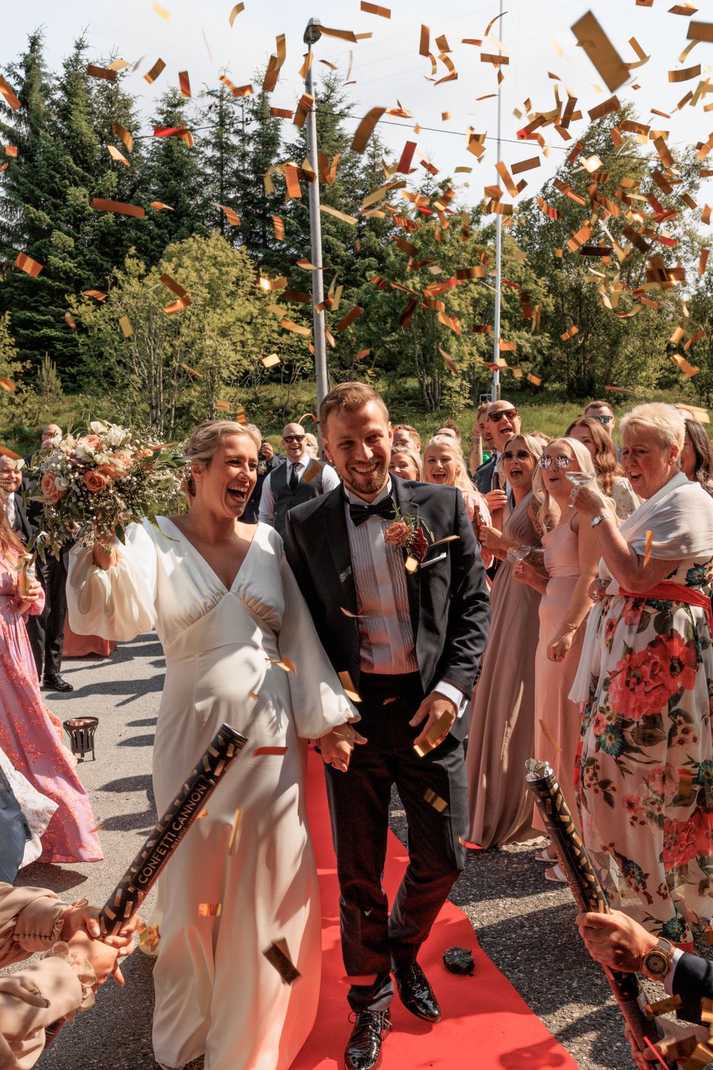Joyful wedding exit with copper confetti raining down on red carpet.