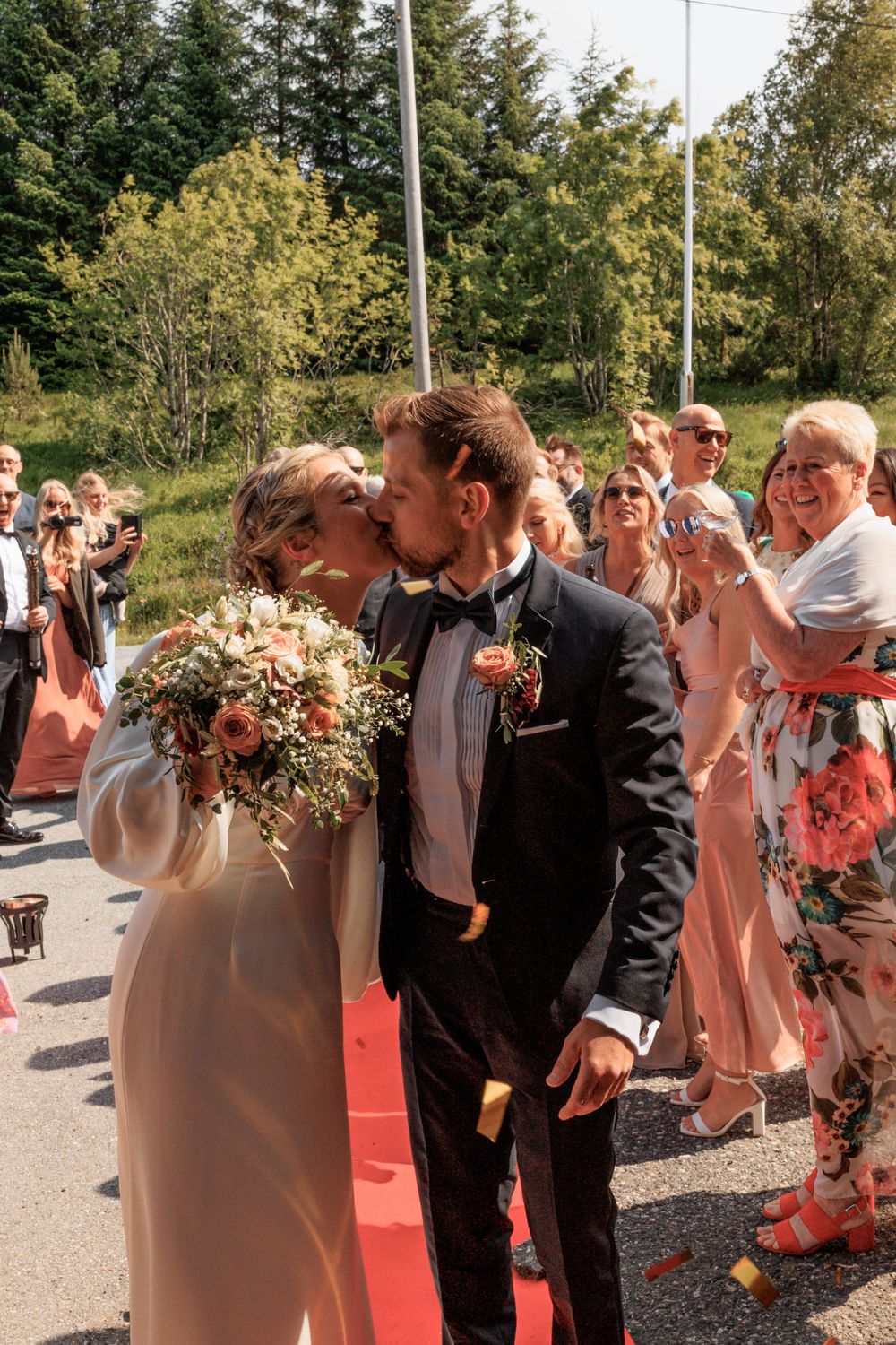 Romantic moment on red carpet with guests celebrating in background.