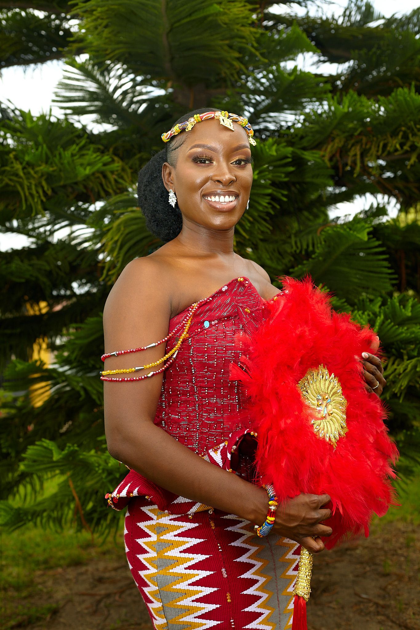 Bride in red beaded dress with feather accessory smiling outdoors.