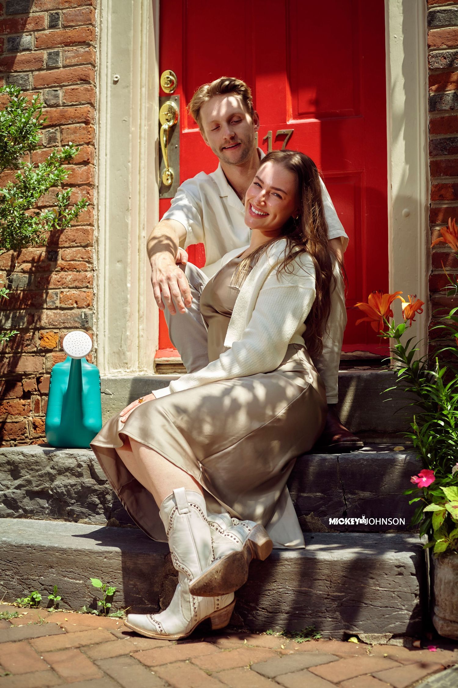 A person in a cream-colored dress sits on brick steps by a red door in an artistic photo series.