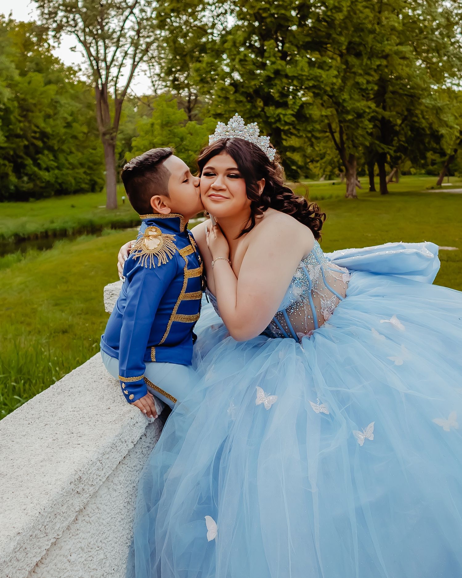 Sweet moment captured in a park setting with light blue ball gown and royal blue military-style suit.