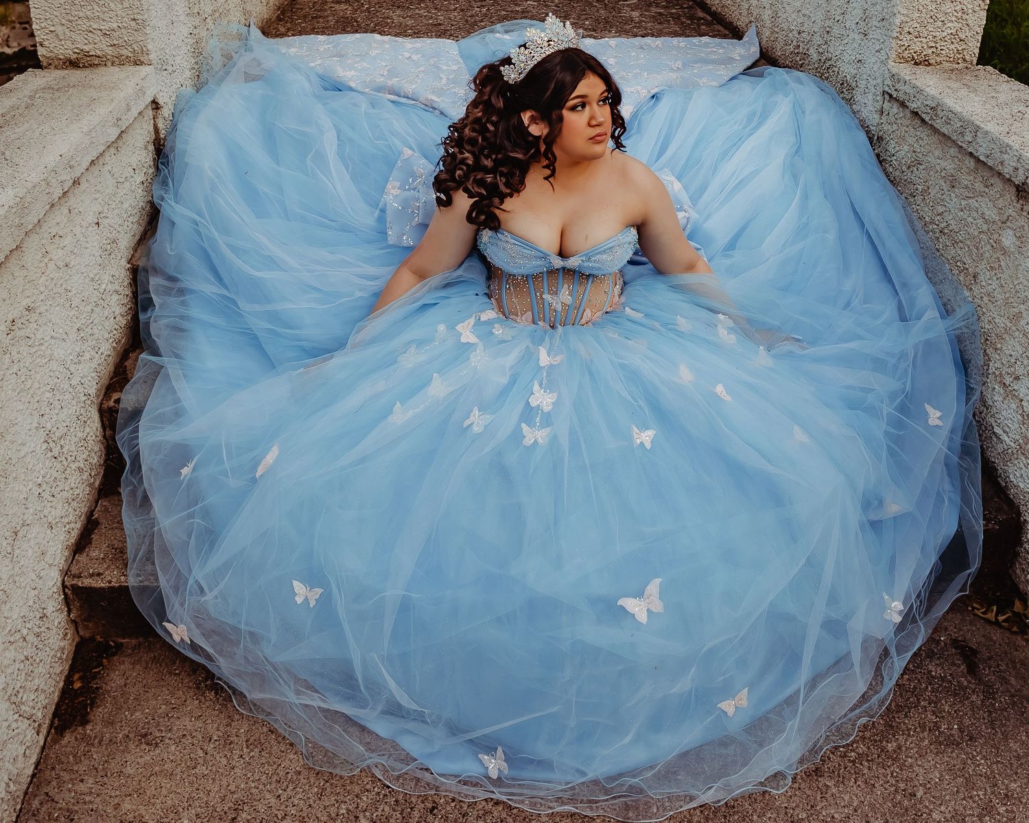 Light blue ball gown with butterfly details photographed on stone steps.