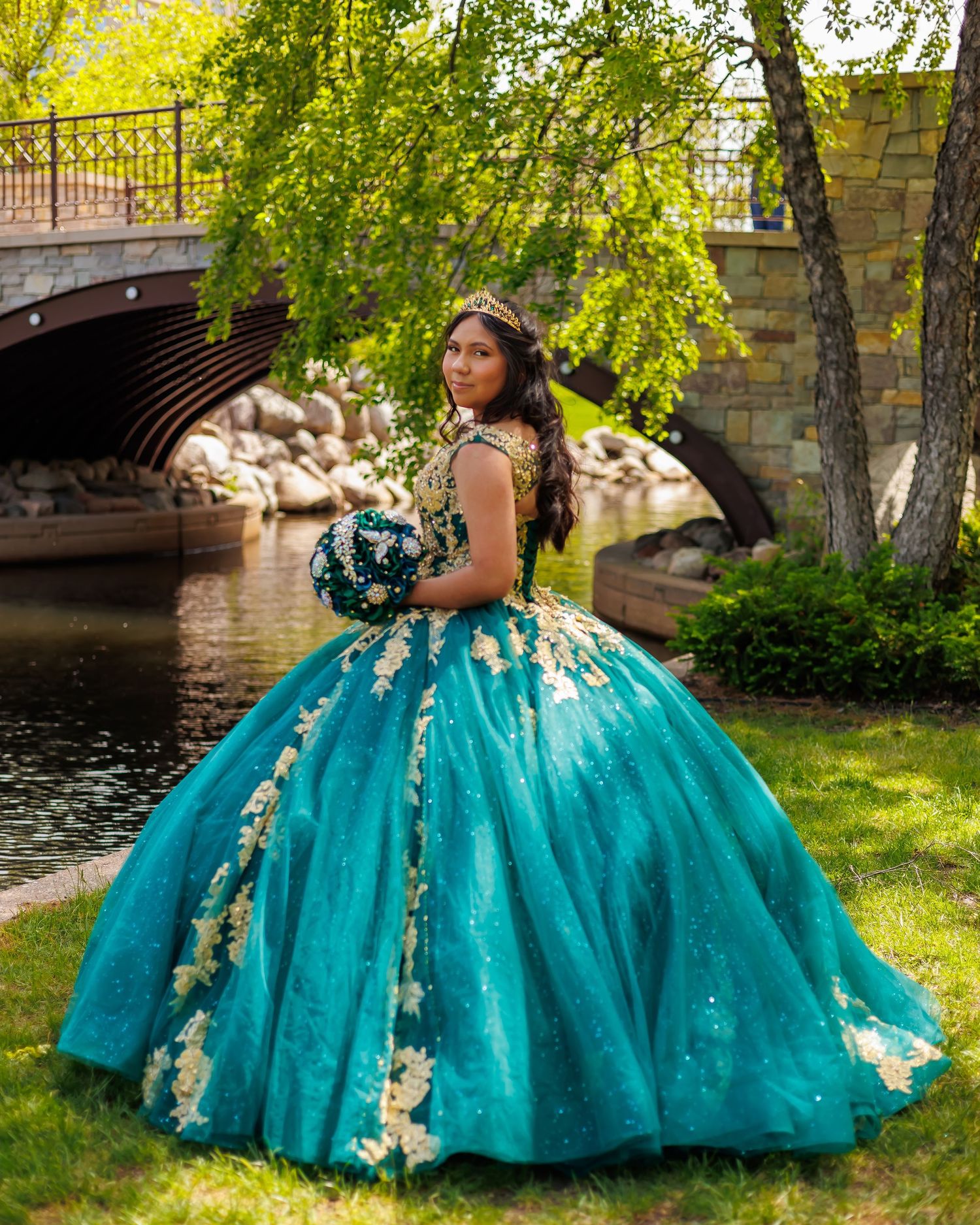 Elegant turquoise ball gown with floral details photographed by stone bridge and water.