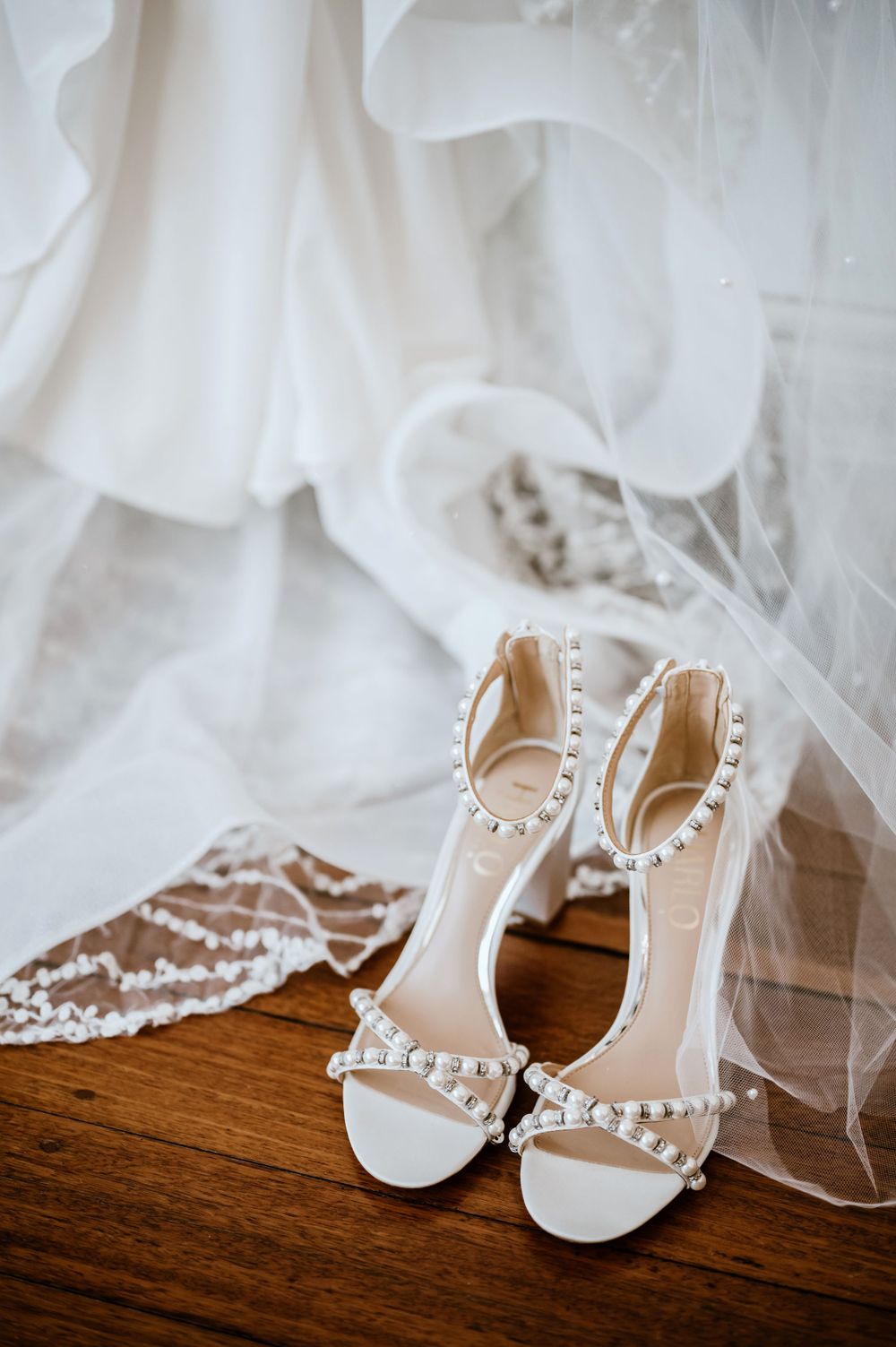 Elegant white bridal shoes with pearl details displayed with wedding dress tulle.