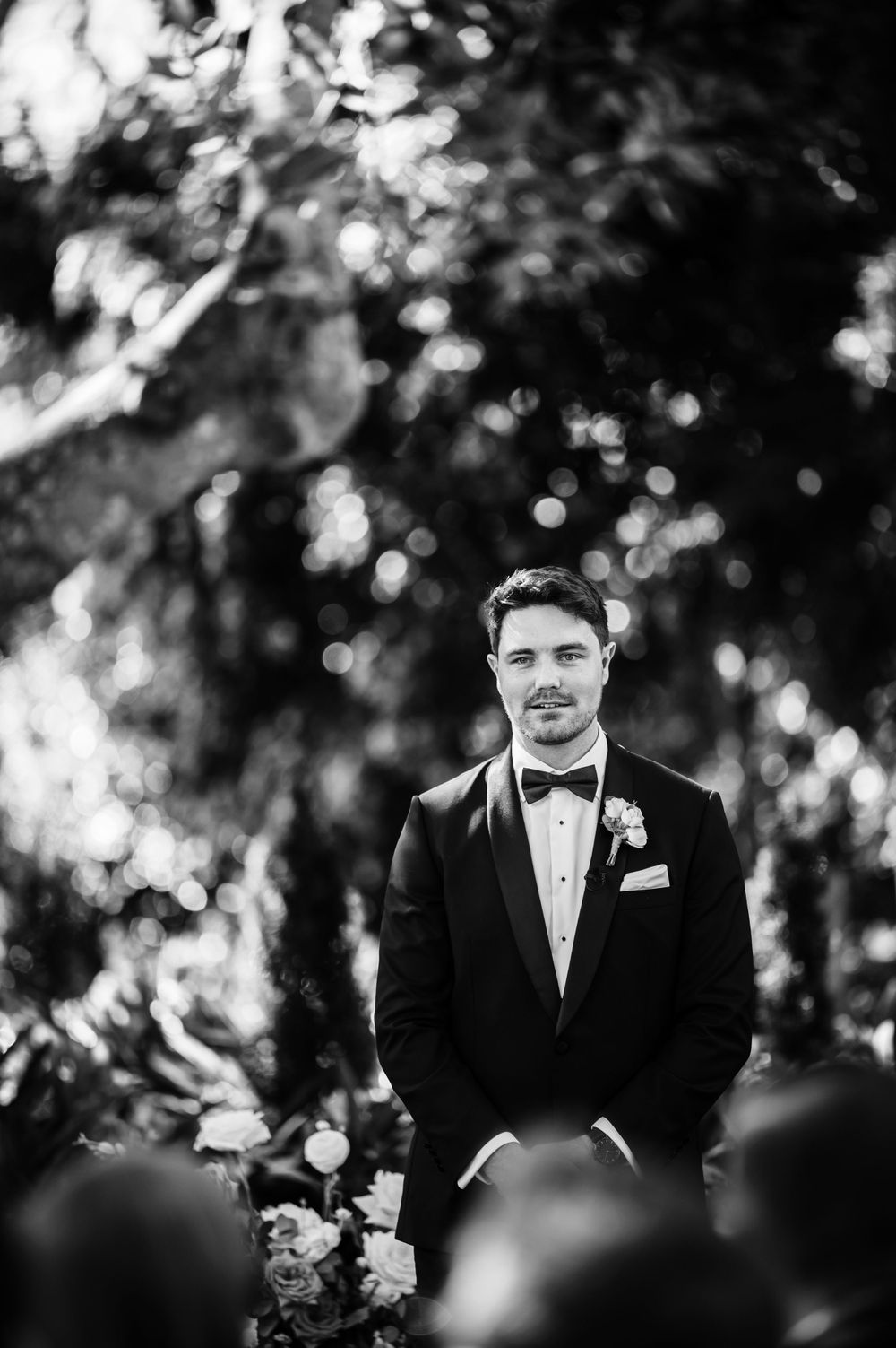 Black and white portrait of groom in classic tuxedo standing outdoors.