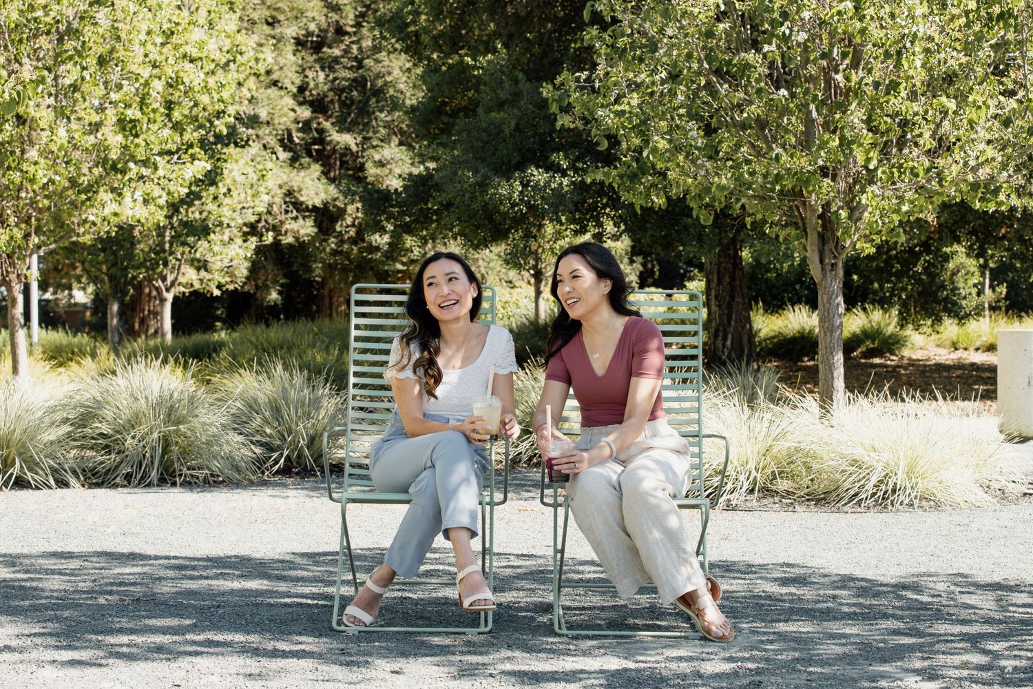 Two people sharing laughs while sitting on outdoor chairs in a sunny garden setting.