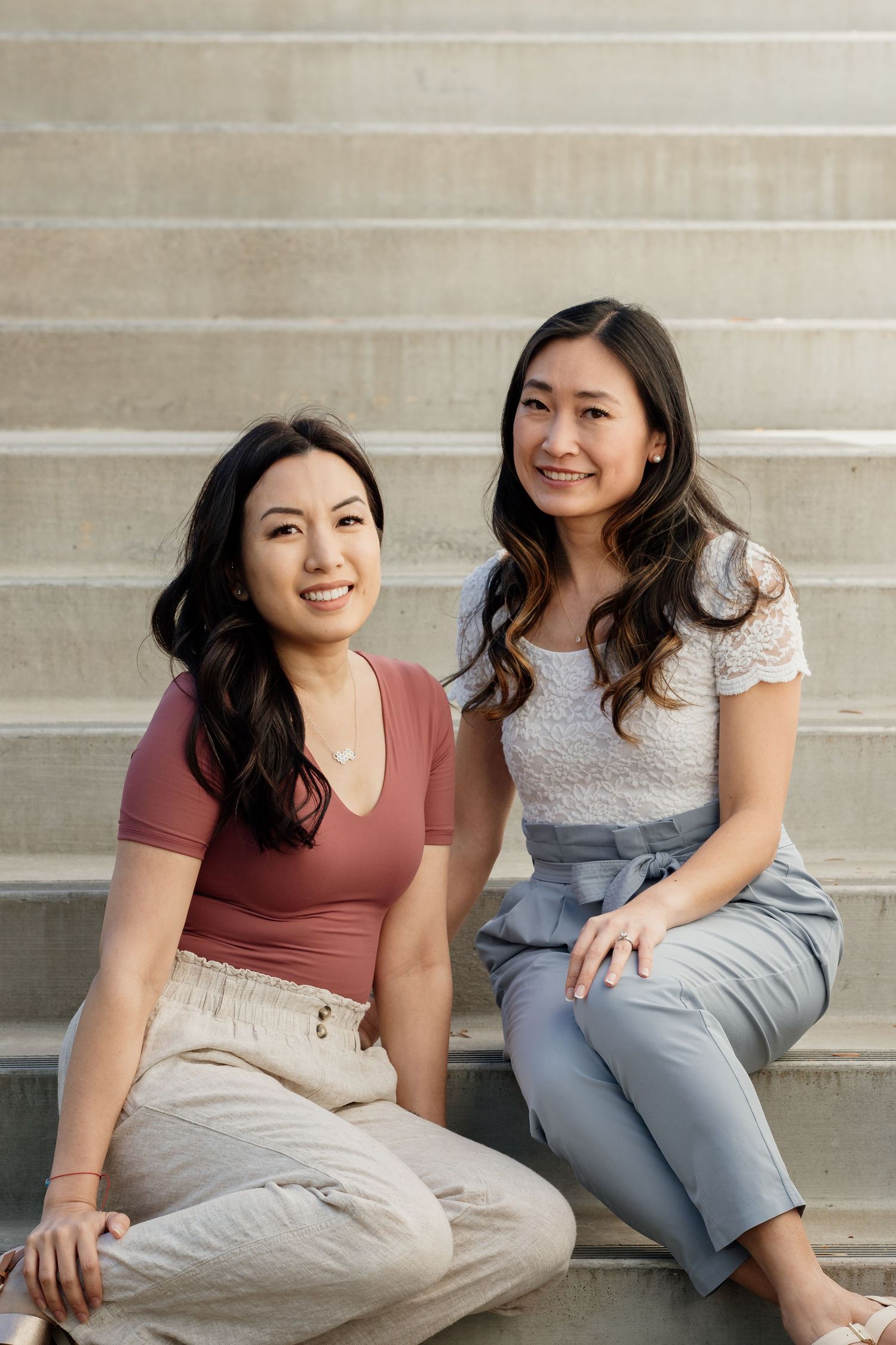 Two friends sitting on concrete steps in coordinated casual outfits.