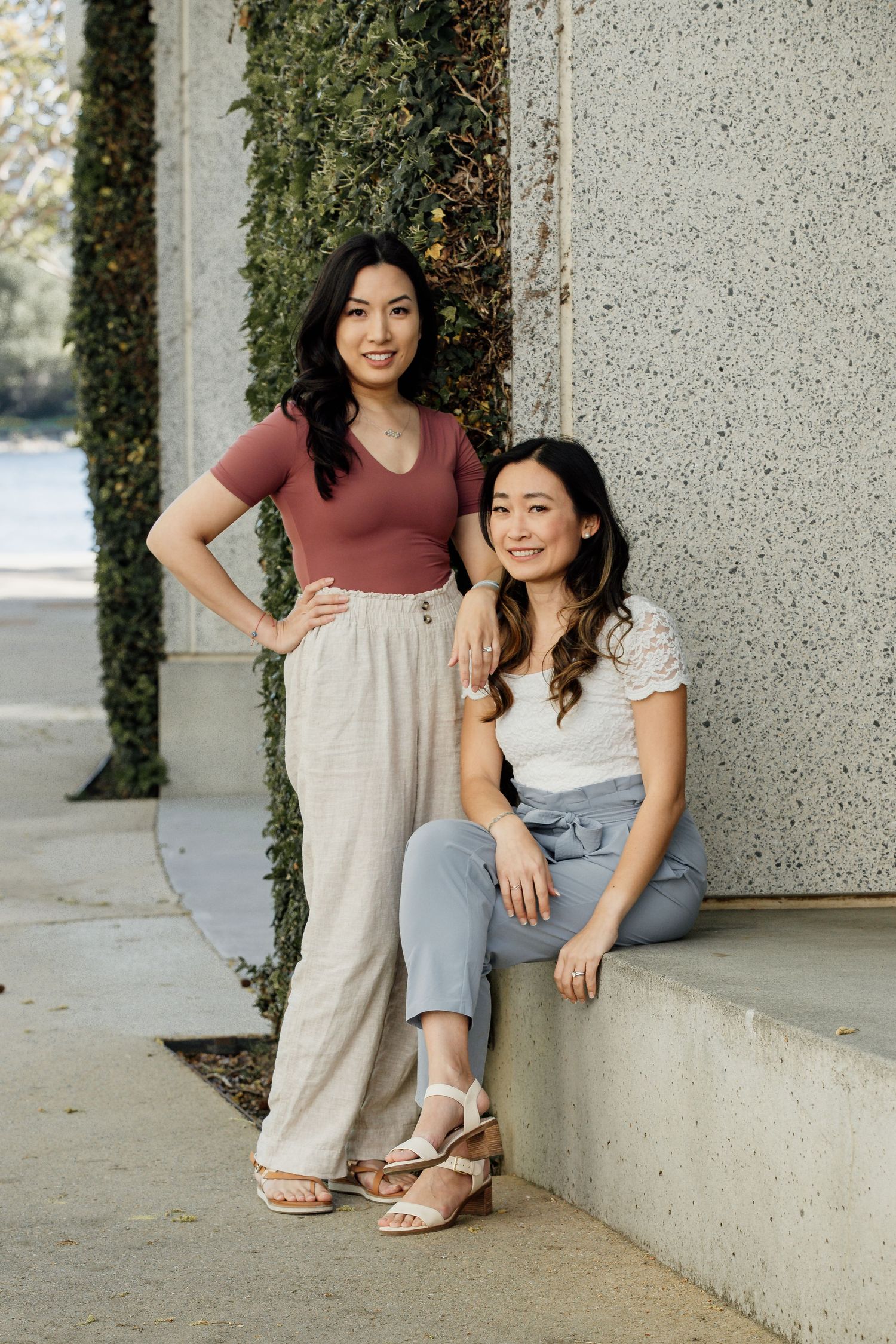 Casual lifestyle portrait of two friends posing against architectural wall with greenery.