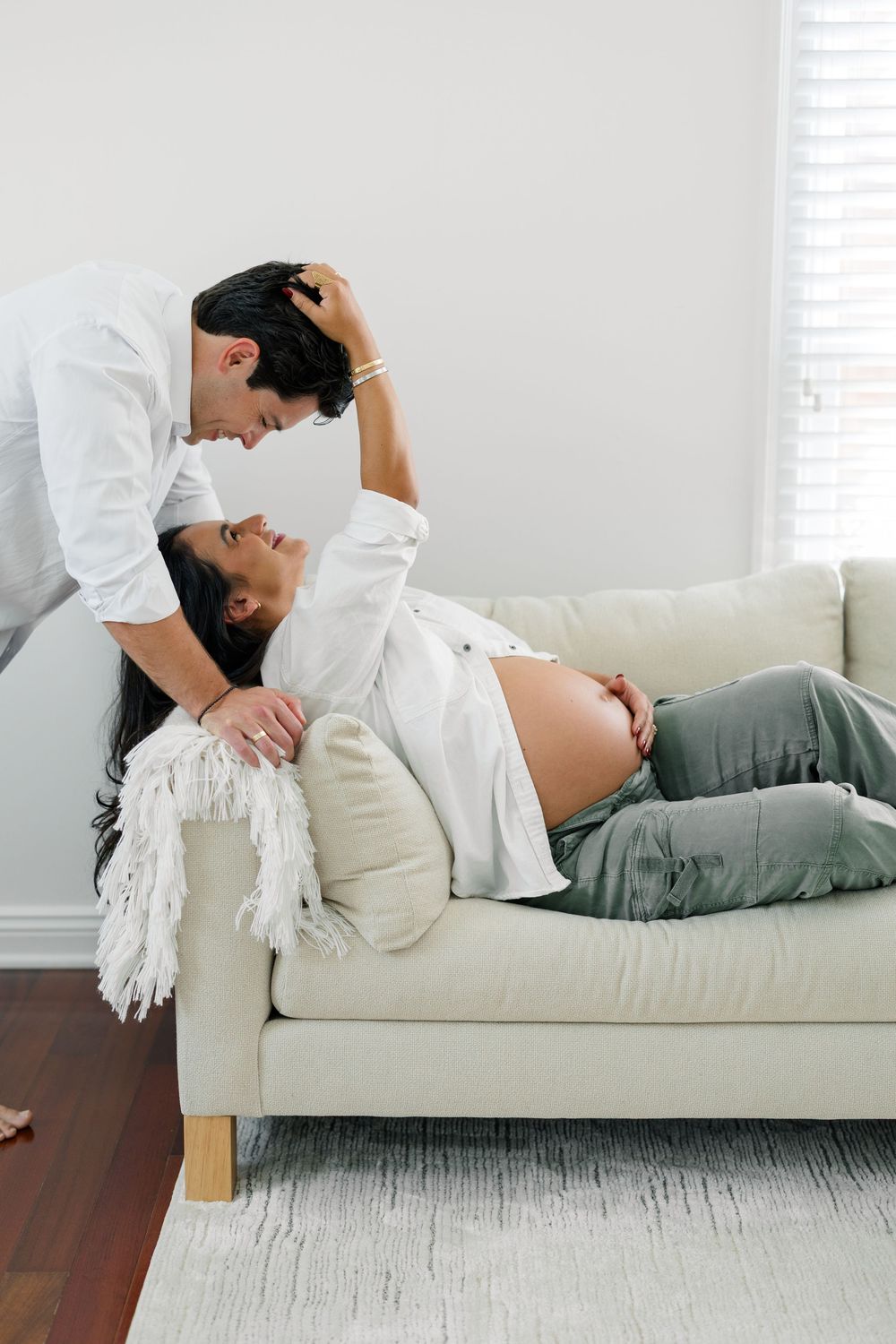A person lies on a white couch wearing a casual outfit in a bright, minimalist room with hardwood floors.