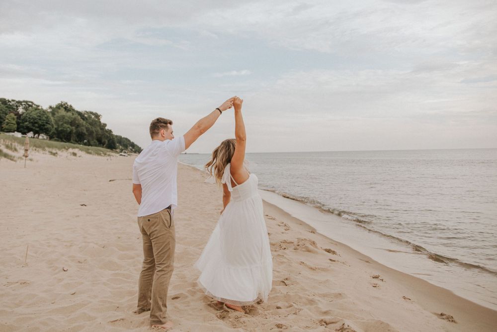 Couple twirling in dance moves along shoreline at sunset.