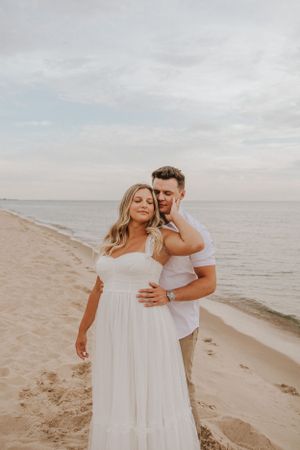 Couple in white sharing intimate embrace on beach at sunset.