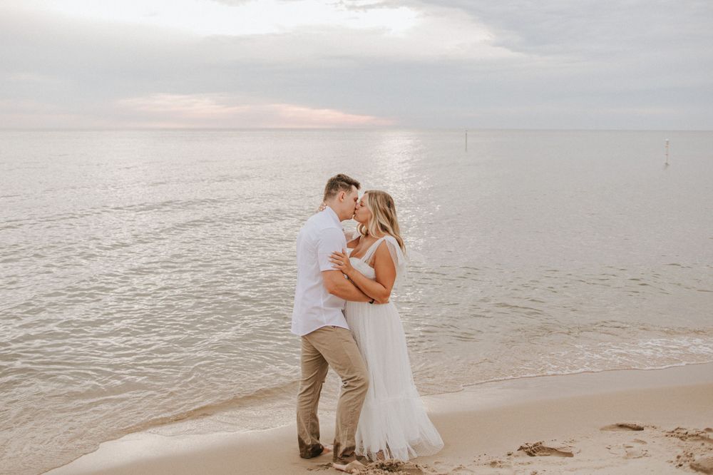 A couple strolls together on a cloudy day at the beach with waves rolling in.