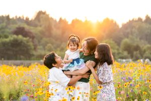 Mother laughing with children in a flower field at sunset.