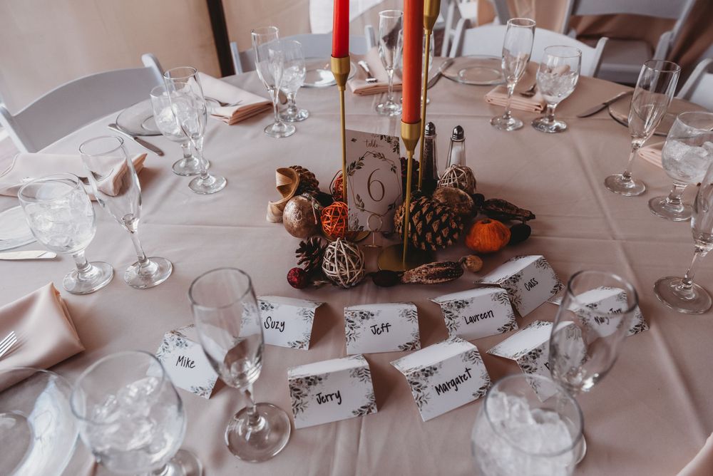 Elegant wedding reception table setting with white linens, wine glasses, and red taper candles in brass holders.