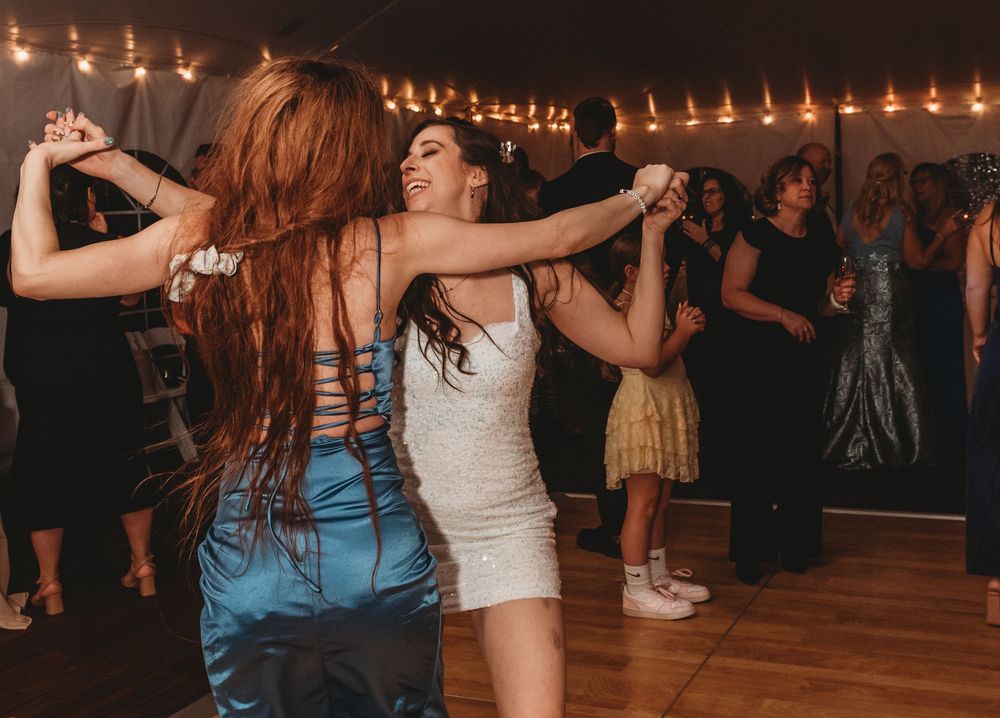 People dancing together on a wooden dance floor under warm string lights at a party celebration.