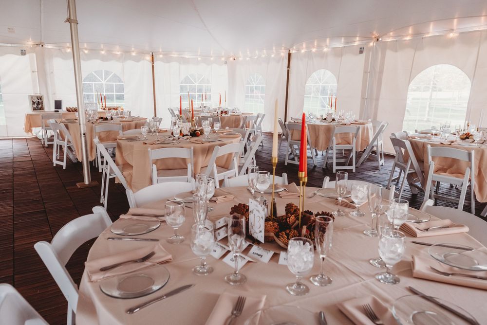 Elegant wedding reception venue with white tablecloths and place settings under a white tent with natural lighting.