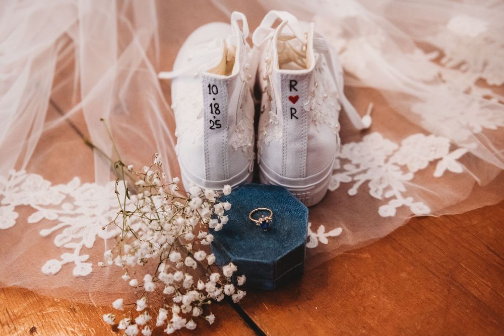 White baby shoes and delicate baby's breath flowers arranged on a wooden surface with soft tulle fabric.