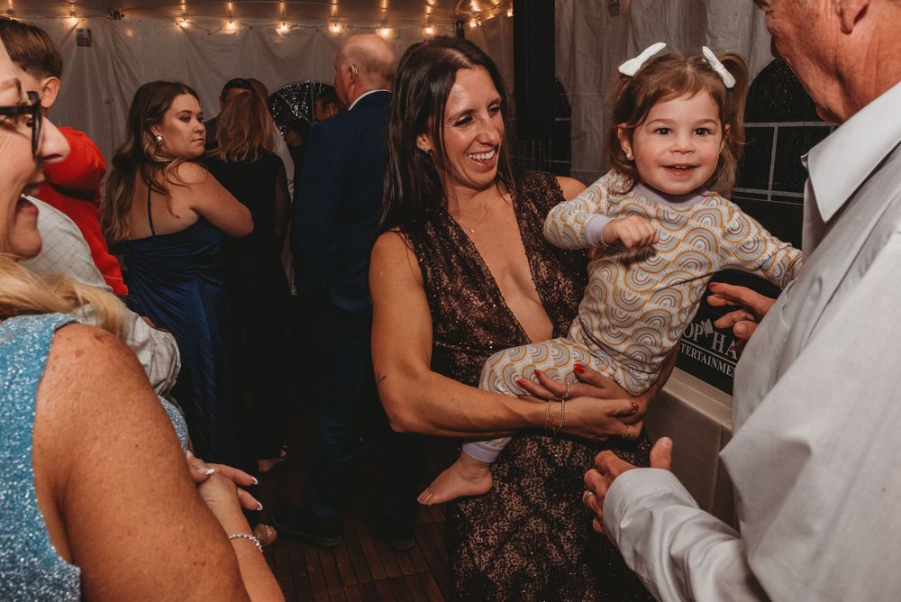 People dancing and celebrating at a lively wedding reception with string lights glowing overhead.