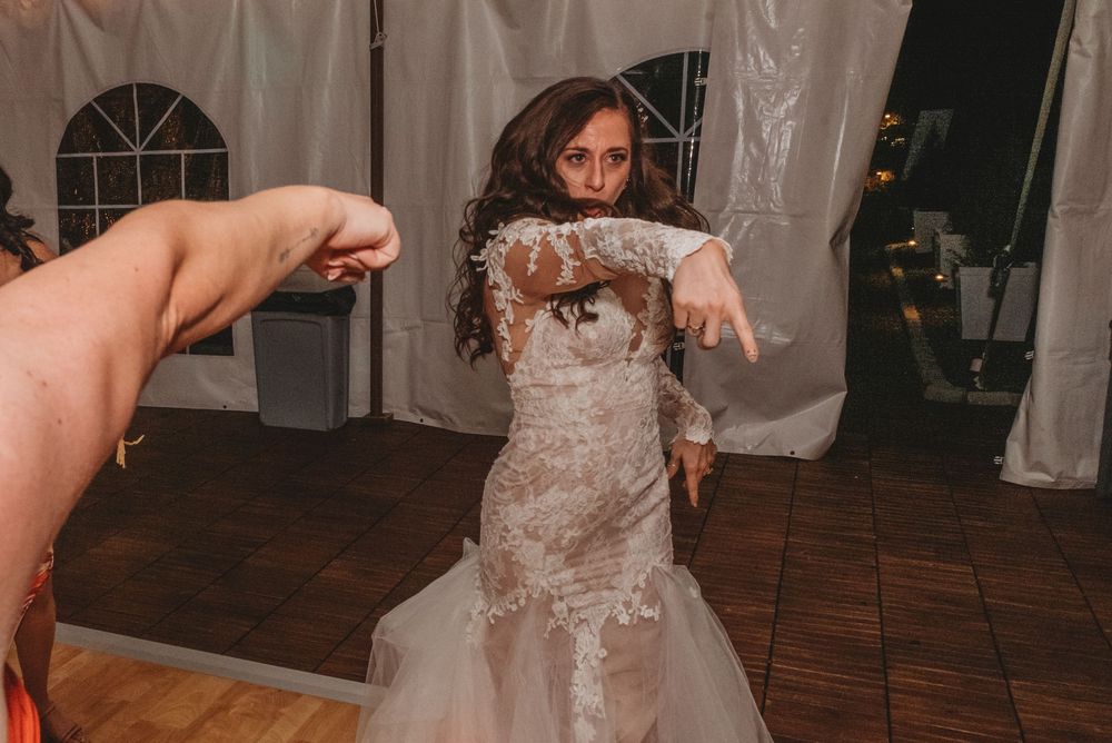 A couple dances together at their wedding reception on a wooden dance floor surrounded by white drapes.