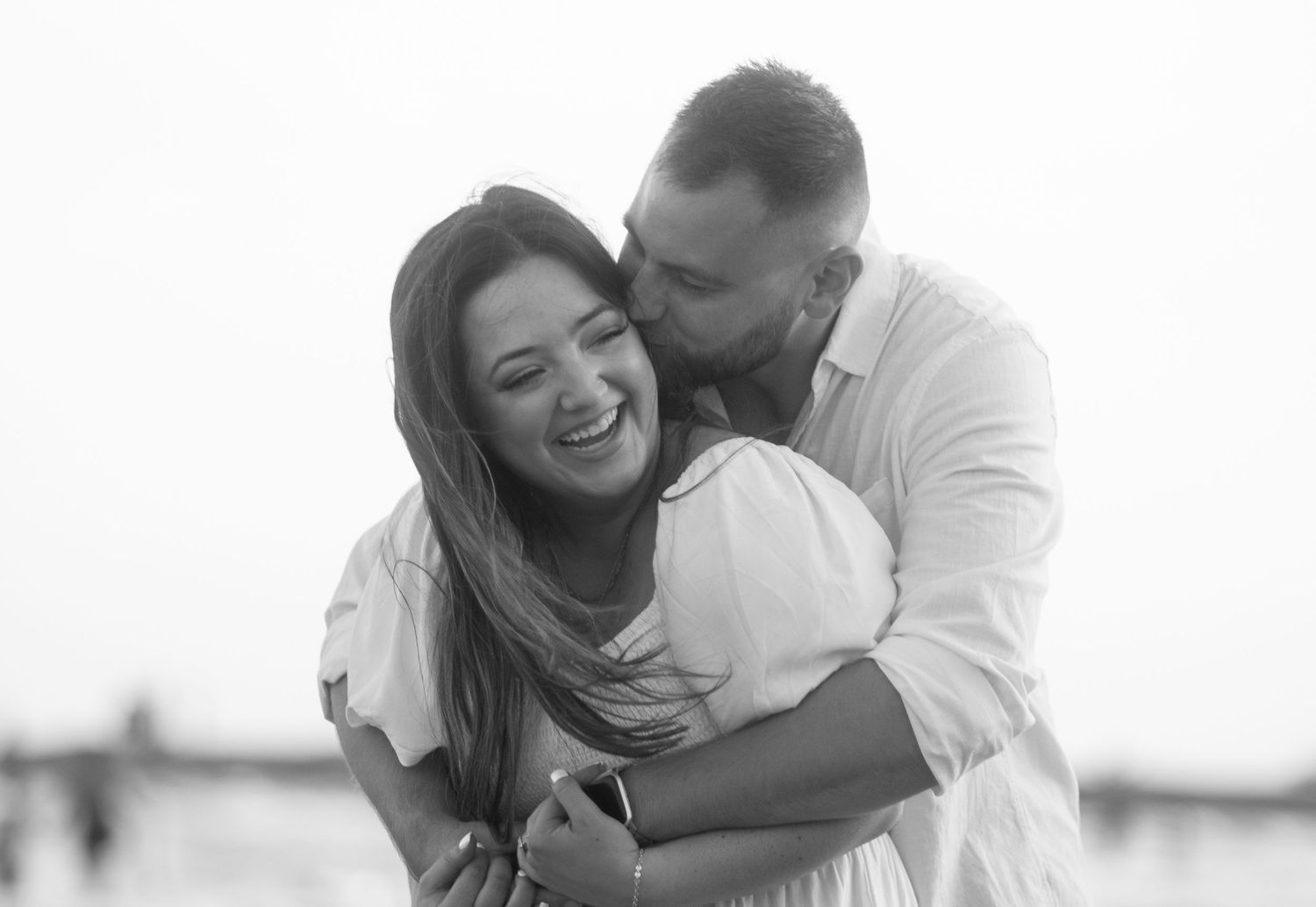 Black and white photo of a couple embracing and laughing together outdoors.