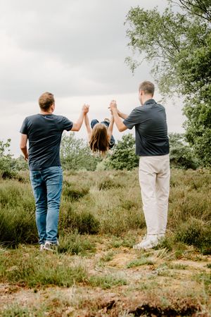 Family members holding hands and swinging together in a natural outdoor setting.