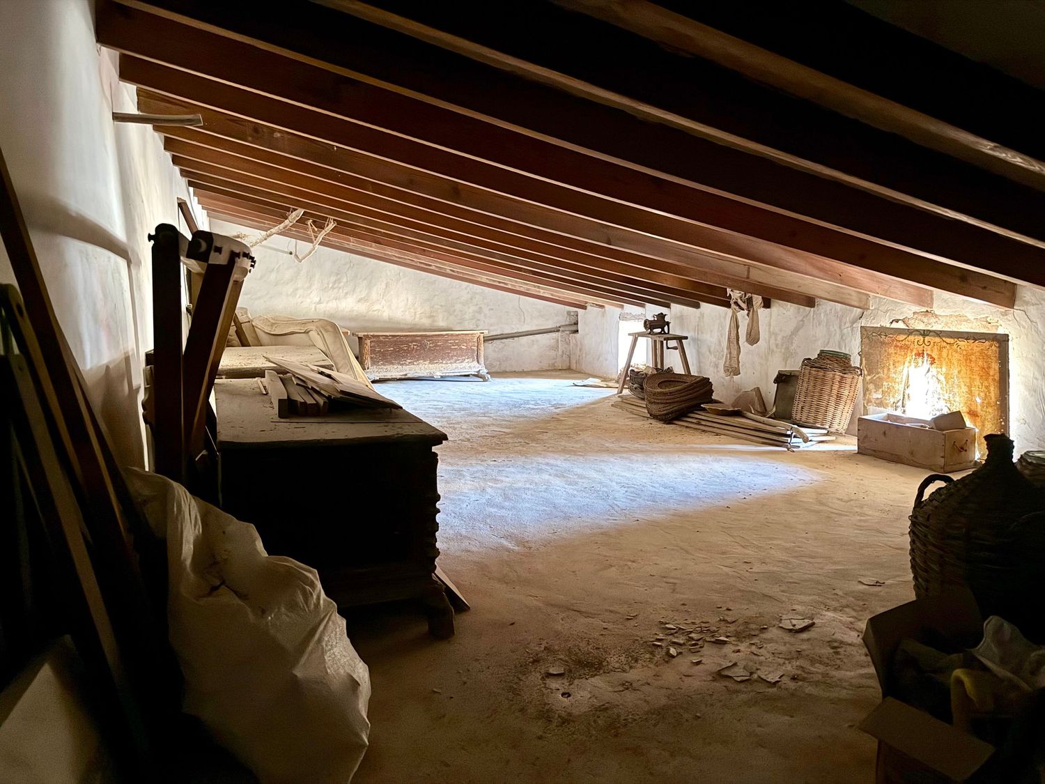Spacious unfinished attic storage area with exposed wooden beams, dirt floor, and white insulation walls.