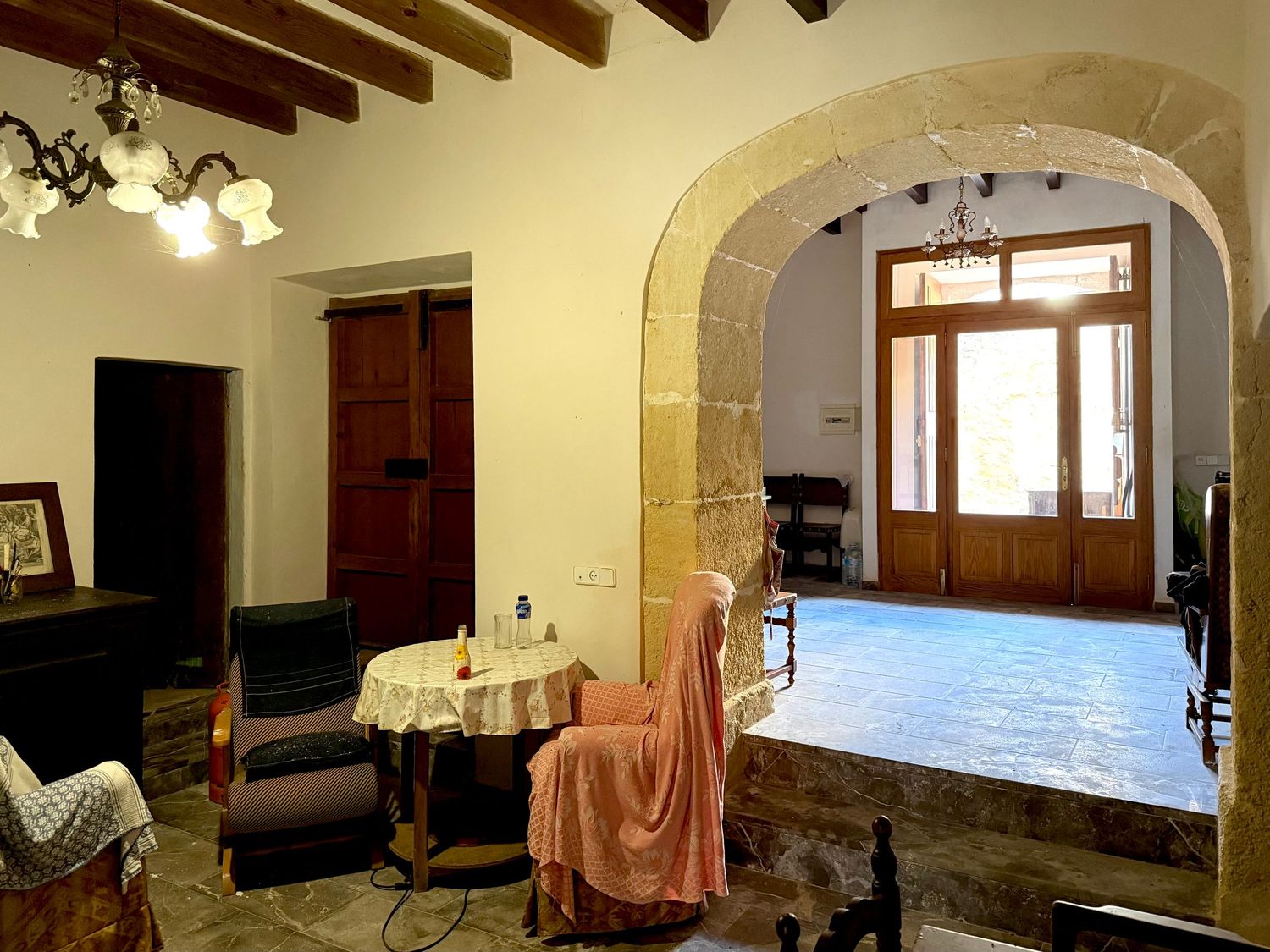 Rustic Mediterranean interior with stone archway, wooden beamed ceiling, terracotta floors, and elegant antique furnishings.