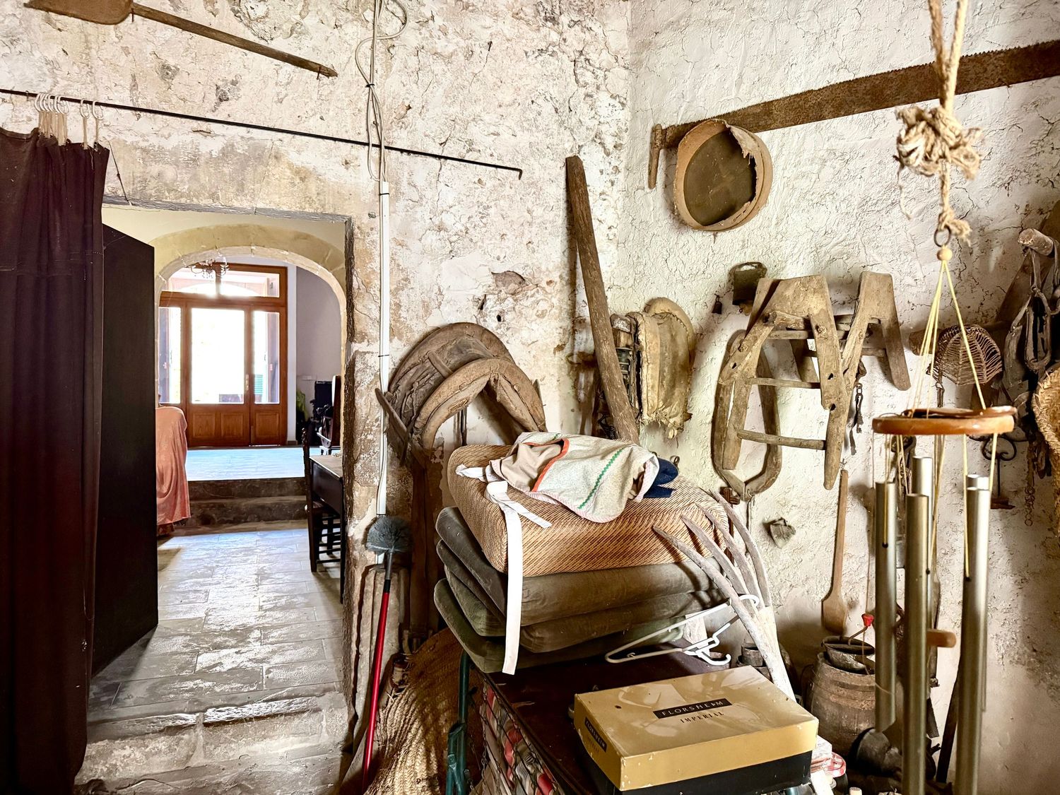 Rustic stone room with antique saddles, horse tack, and vintage items stored in a historic building.