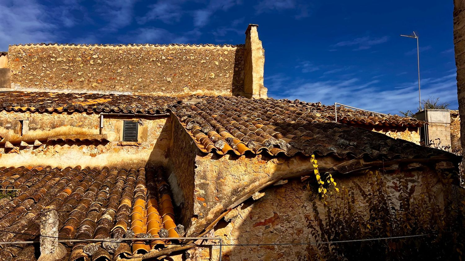 Ancient stone building with terracotta roof tiles under a vivid blue sky in a rustic Mediterranean village.