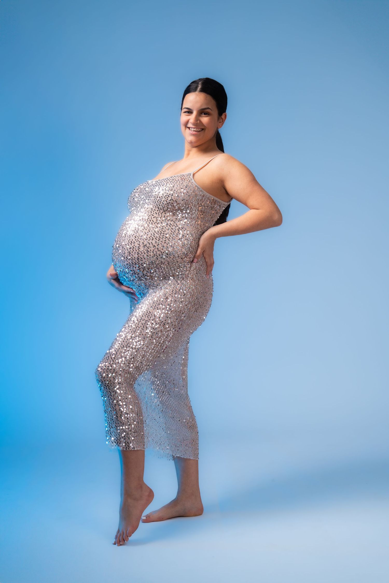 Woman in sparkly silver dress poses playfully against blue background.