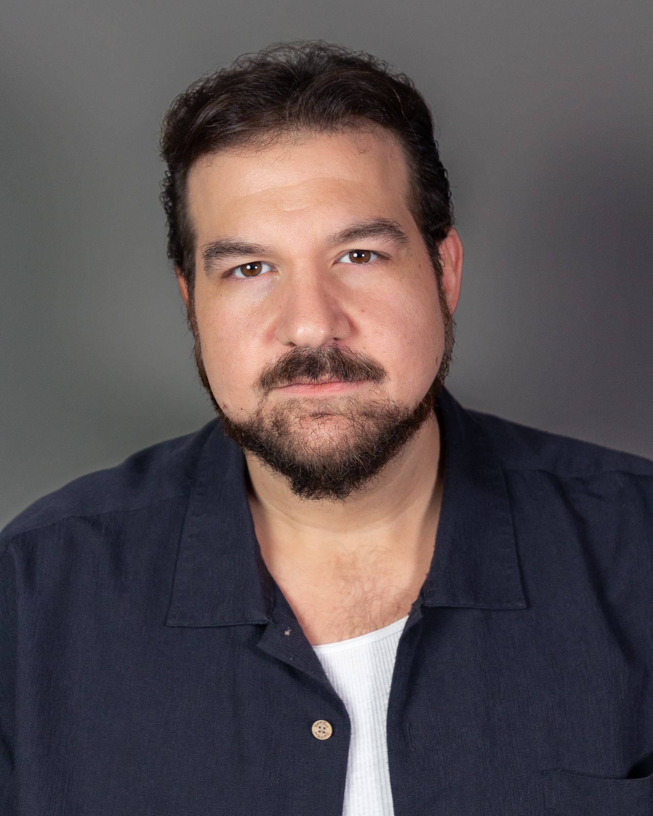 Professional headshot of a man in navy shirt against grey background.