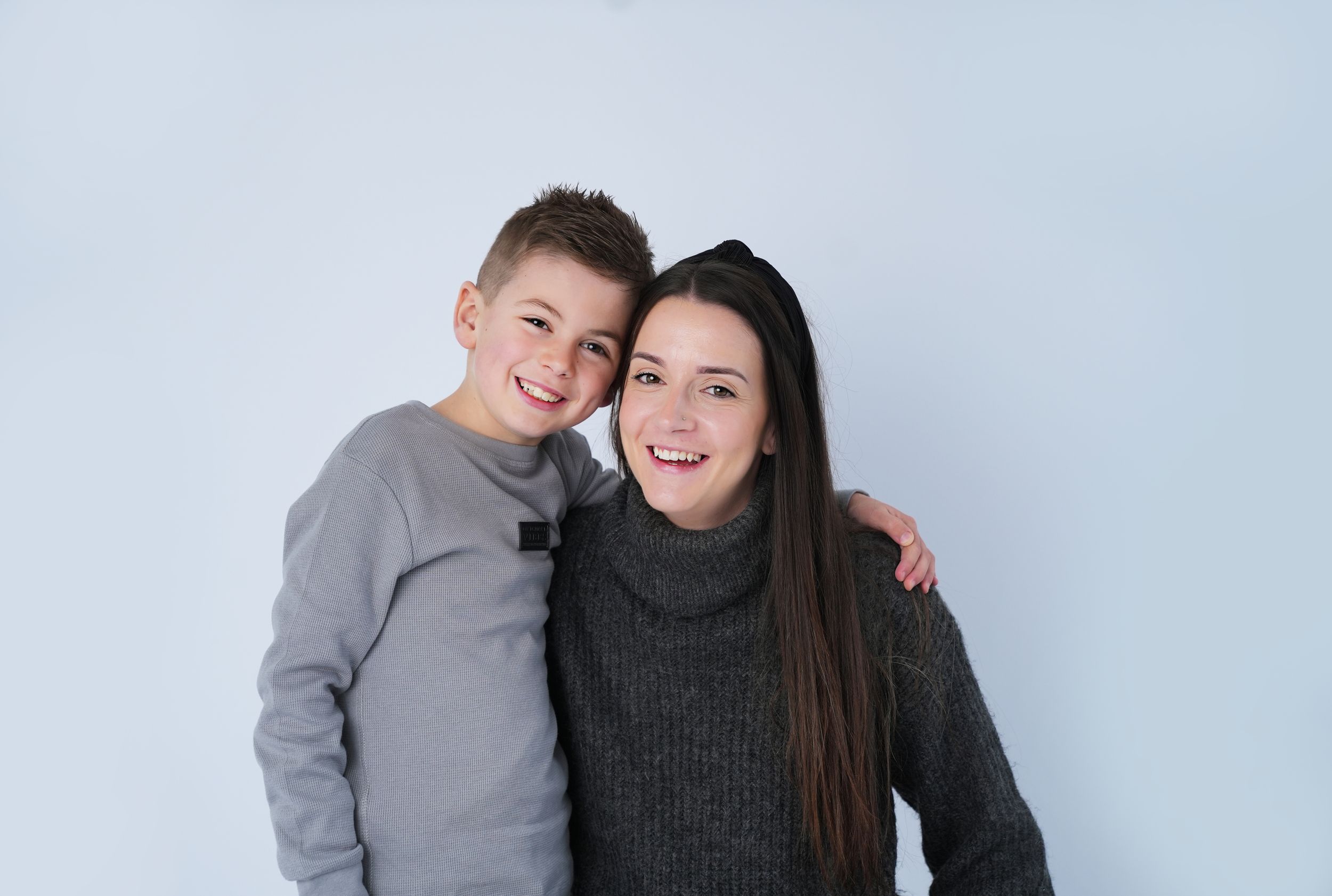 A pair in casual winter sweaters pose together against a light blue background.