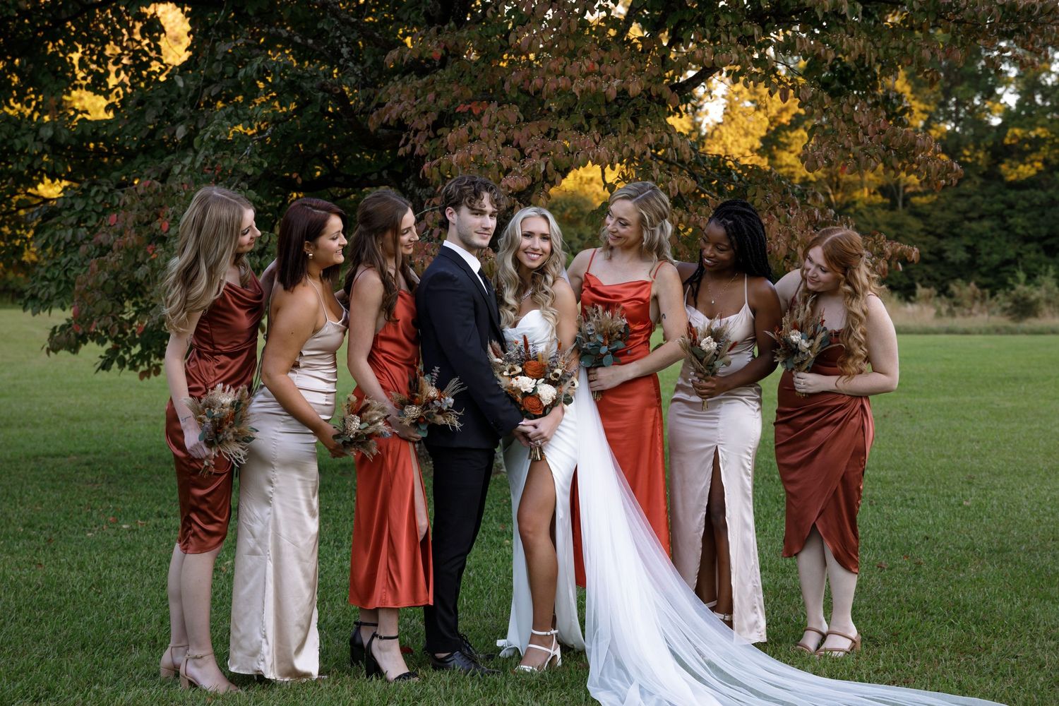 Wedding party poses outdoors in a scenic garden setting during golden hour.