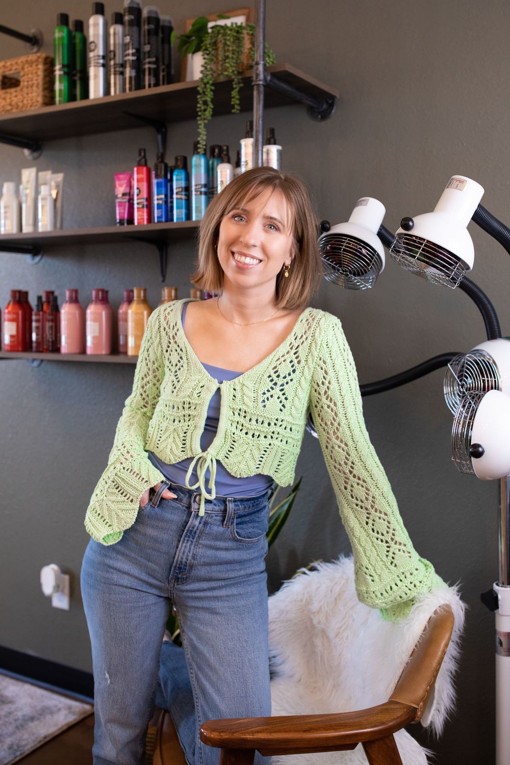 Truly Juli Photography headshot of a hair salon owner posing next to a hair dryer with colorful hair product bottles in the background