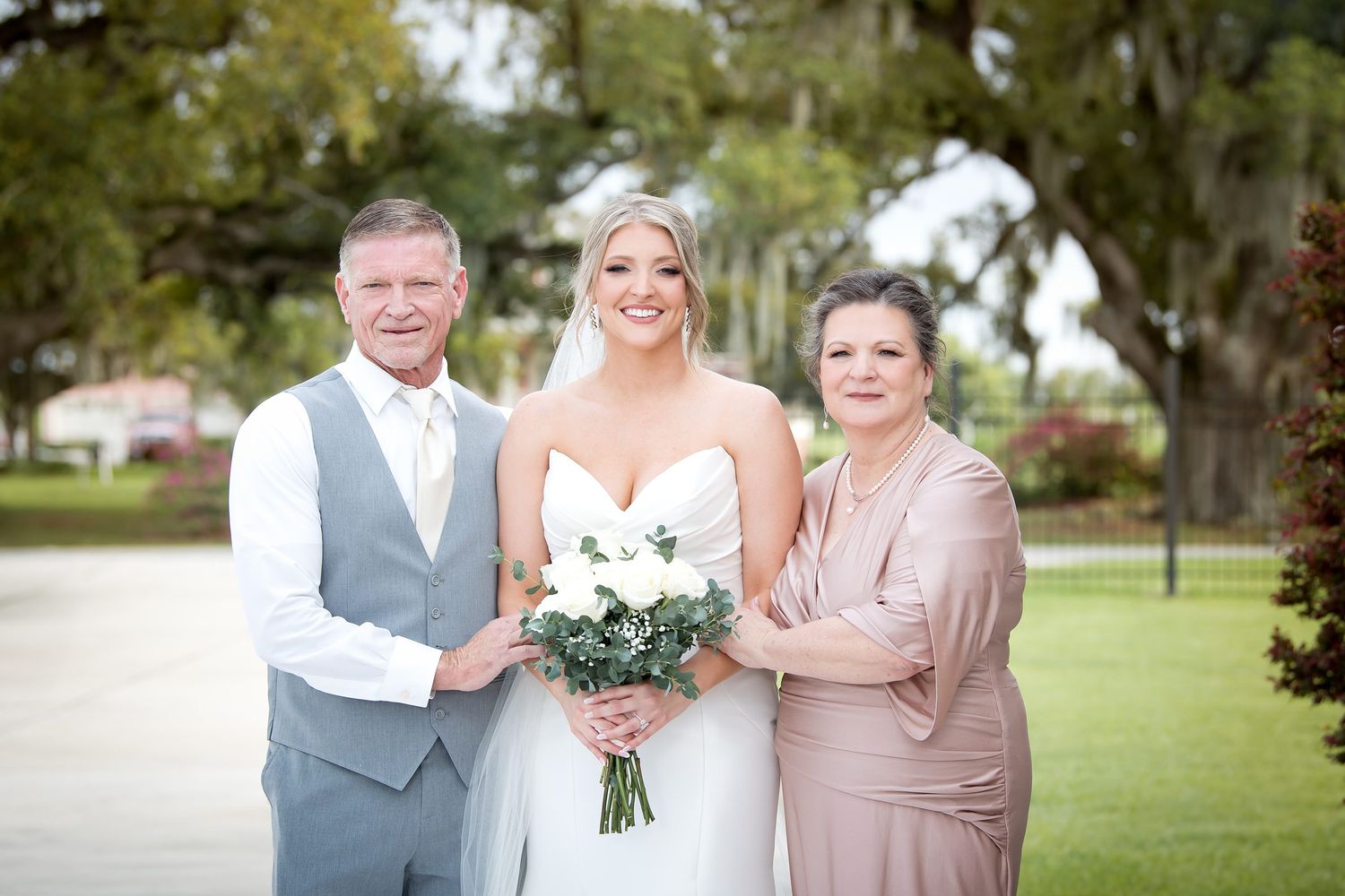 Wedding party members in gray suits and blush dresses pose together outdoors on a sunny day.