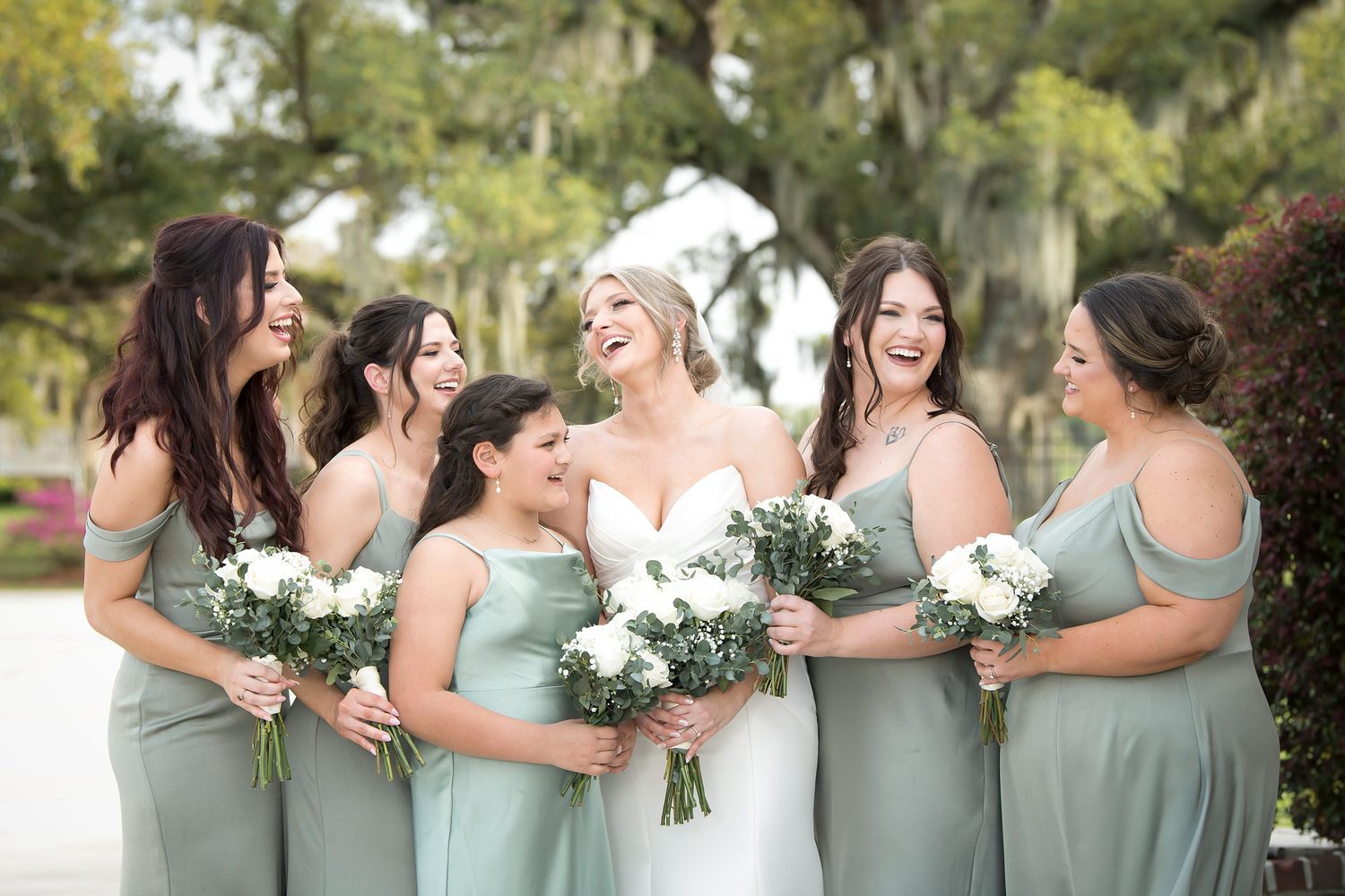 Bridesmaids in soft mint green dresses pose together holding white bouquets.