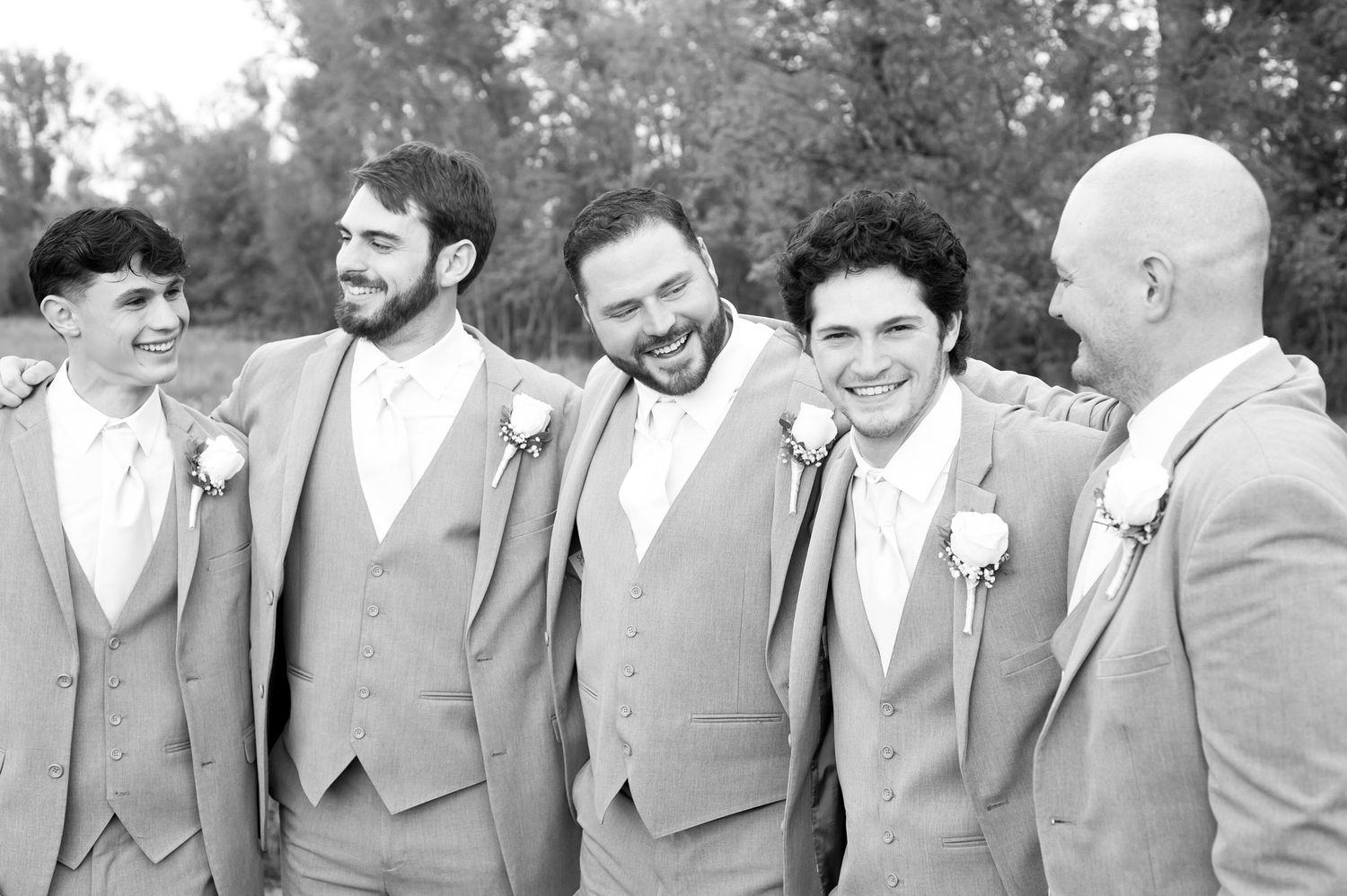 Groomsmen in coordinated gray suits and white ties share candid moments outdoors.