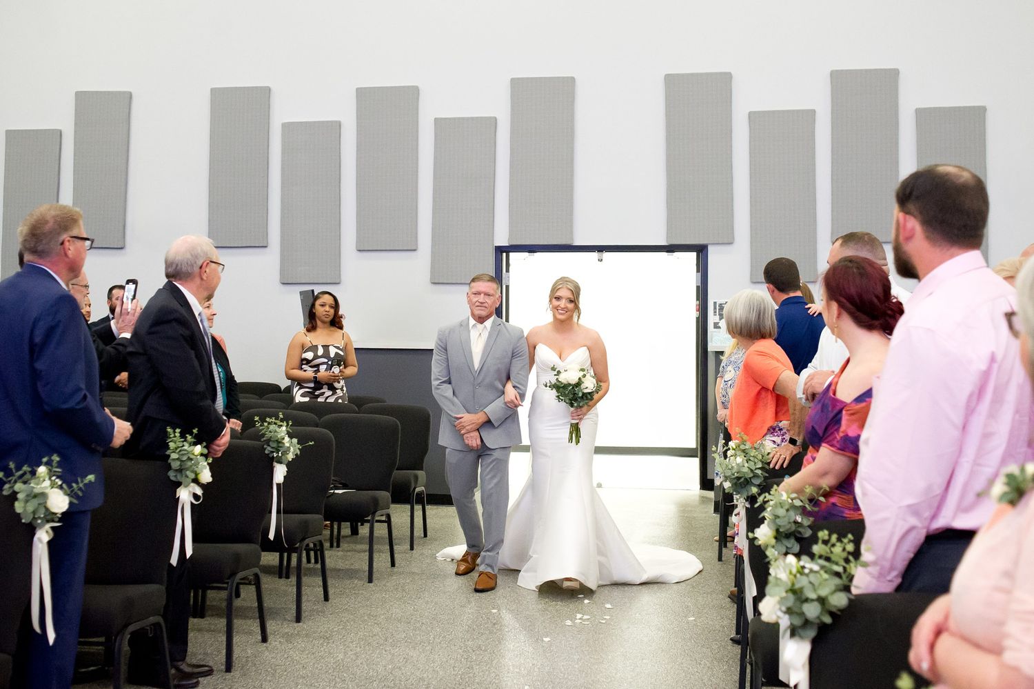 Wedding ceremony in modern white church interior with rows of chairs.
