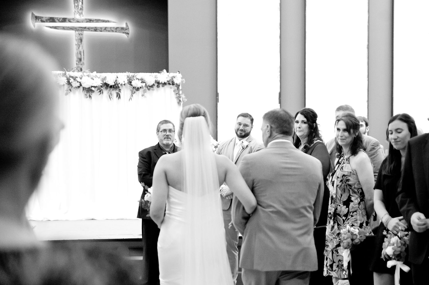 Wedding ceremony in progress with illuminated cross and floral arch decorations in an elegant indoor venue.