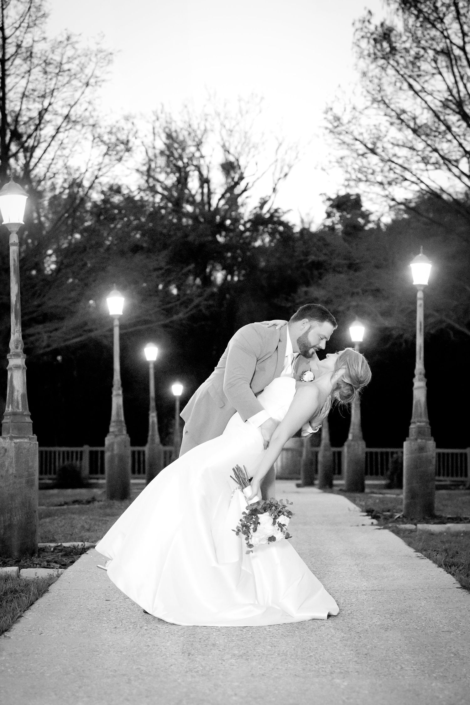 Romantic evening wedding portraits under lamp posts in a park setting.