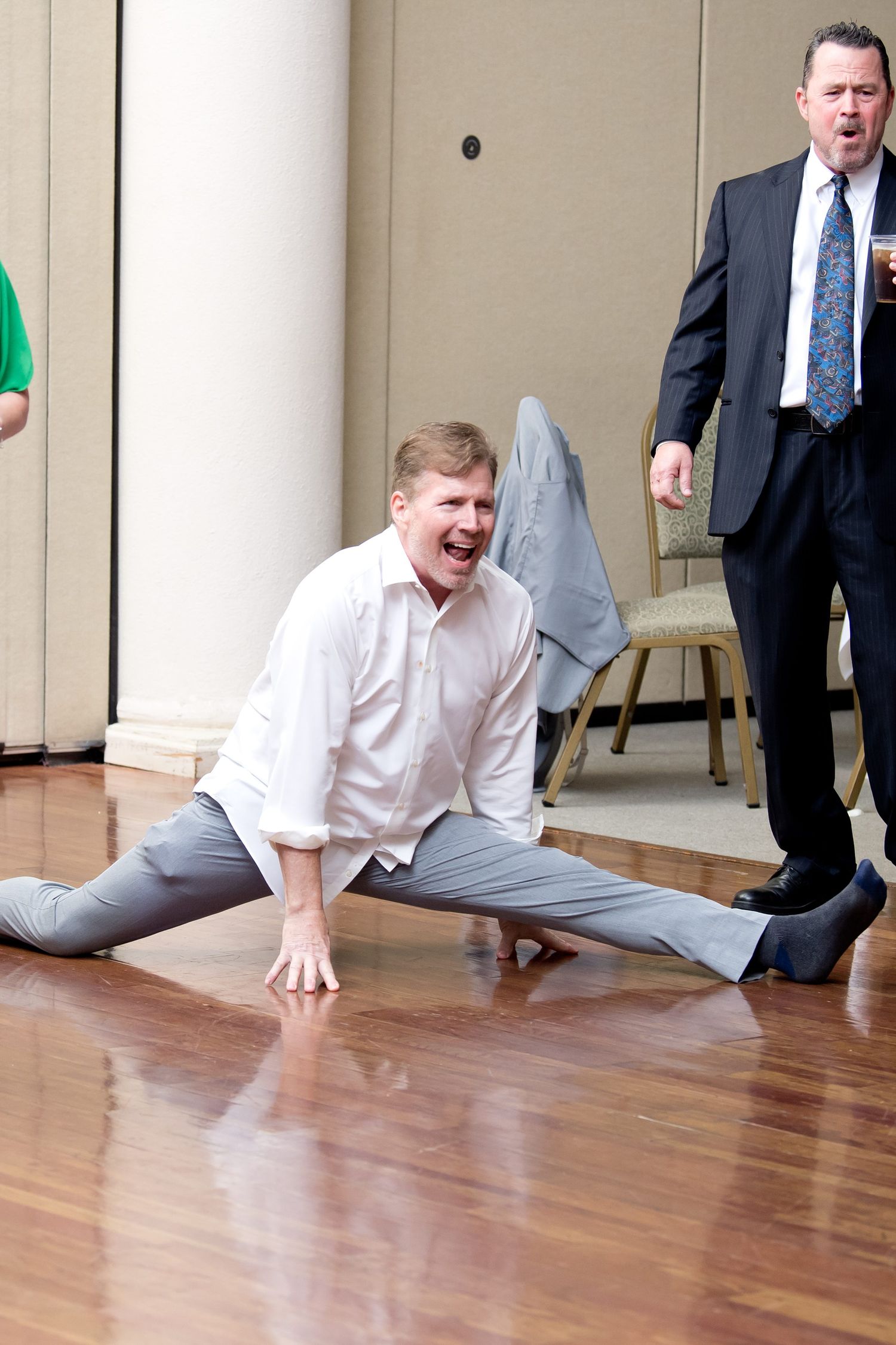 Person performing splits on wooden dance floor during wedding reception celebration.