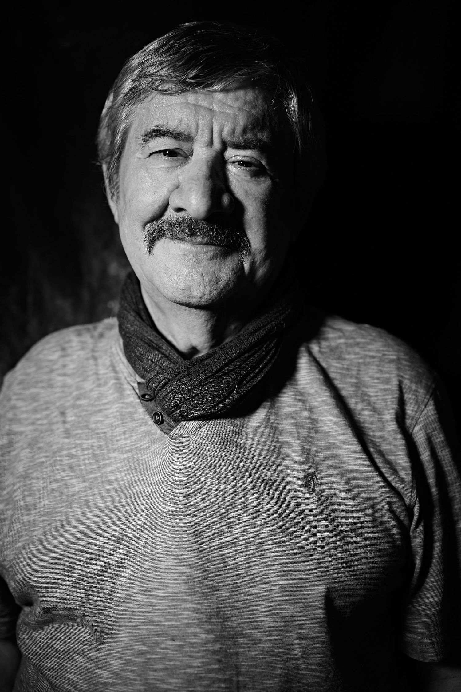 Black and white portrait of older man in gray sweater and scarf with distinguished mustache.
